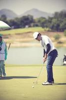 jugador de golf en el putting green golpeando la bola en un agujero.color vintage foto