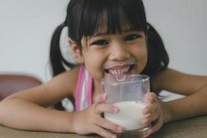 la niña asiática está bebiendo leche de un vaso, estaba muy feliz. foto