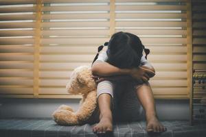 Close up lonely little girl hugging toy, sitting at home alone, upset unhappy child waiting for parents, thinking about problems, bad relationship in family, psychological trauma photo