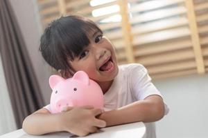 Little Asian girl saving money in a piggy bank, learning about saving, Kid save money for future education. Money, finances, insurance, and people concept photo