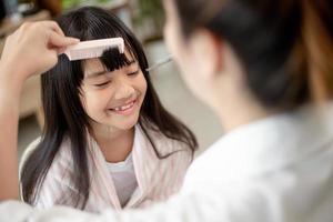 Asian Mother cutting hair to her daughter in living room at home while stay at home safe from Covid-19 Coronavirus during lockdown. Self-quarantine and social distancing concept. photo