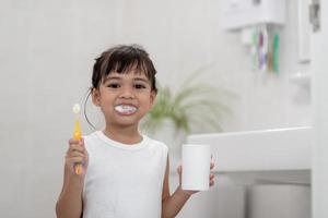 pequeña y linda niña limpiándose los dientes con un cepillo de dientes en el baño foto