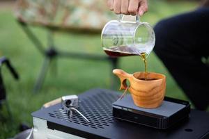 Young man pouring coffee in cup, morning breakfast on open air. traveler camping for first time, new experience to rest with tent. Nature, leisure, no rush, peace and calmness concept photo