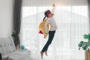 Girls child jumping on home living room couch wearing improvised superhero outfit fancy dress, playing having fun with energetic games, indoors. Discovery kids activities holiday lifestyle. photo