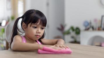 happy little Asian girl learning to clean with a rag in the living room at home. housework and household concept. photo