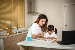 feliz madre e hija sonriente juntas pintando con marcadores. madre ayudando a su hijo adoptado con la tarea de arte. madre alegre y niña asiática haciendo pintura en casa. foto