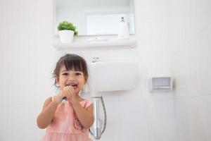 niñita linda limpiándose los dientes con cepillo de dientes en el baño foto