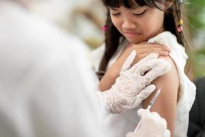 concepto de vacunación. doctora vacunando a una niña linda en la clínica foto