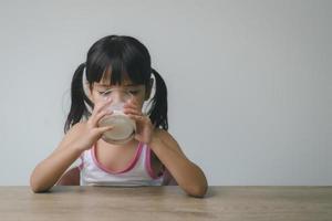 la niña asiática está bebiendo leche de un vaso, estaba muy feliz. foto