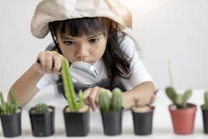 kid gently touch new stem of the cactus he grows with care, one hand holds magnifying glass.Nature education, Montessori and observation skills concept. photo