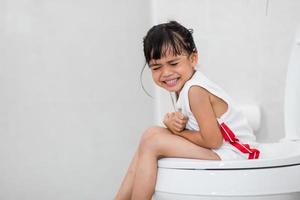 The little girl is sitting on the toilet suffering from constipation or hemorrhoid. photo