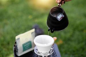 Young man pouring coffee in cup, morning breakfast on open air. traveler camping for first time, new experience to rest with tent. Nature, leisure, no rush, peace and calmness concept photo