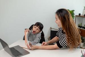 Asian little young girl kid learning online class at home with mother. Preschool child use laptop computer do homework, homeschool from school teacher by digital remote internet with support from mom. photo