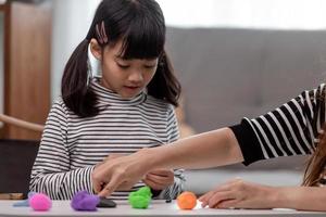 Asian mother and daughter play modeling clay together in kitchen with day light and they look happy. Concept of enjoy with family time photo