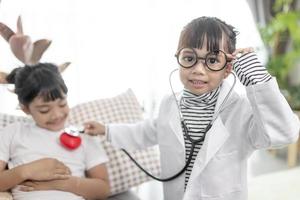 Two cute children play doctor and hospital using stethoscope. Friends girls having fun at home or preschool.