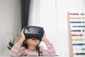 niño con casco de realidad virtual sentado detrás de la mesa en casa foto