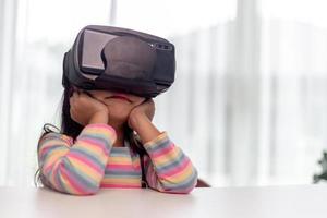 niño con casco de realidad virtual sentado detrás de la mesa en casa foto