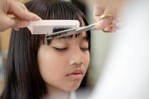 Asian Mother cutting hair to her daughter in living room at home while stay at home safe from Covid-19 Coronavirus during lockdown. Self-quarantine and social distancing concept. photo