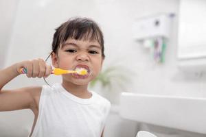 pequeña y linda niña limpiándose los dientes con un cepillo de dientes en el baño foto