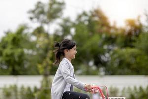 feliz niña alegre montando una bicicleta en el parque en la naturaleza foto