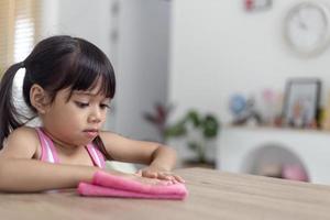 happy little Asian girl learning to clean with a rag in the living room at home. housework and household concept. photo