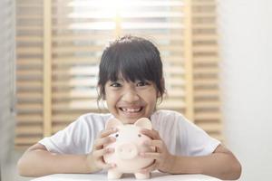 Little Asian girl saving money in a piggy bank, learning about saving, Kid save money for future education. Money, finances, insurance, and people concept photo