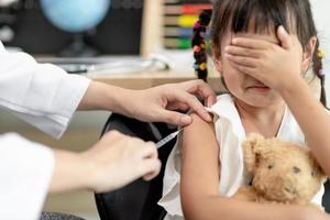 concepto de vacunación. doctora vacunando a una niña linda en la clínica foto