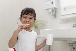 pequeña y linda niña limpiándose los dientes con un cepillo de dientes en el baño foto