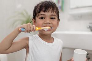 pequeña y linda niña limpiándose los dientes con un cepillo de dientes en el baño foto