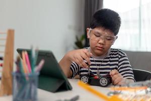 Young asia student remotely learn online at home  in coding robot car and electronic board cable in STEM, STEAM, mathematics engineer science technology computer code in robotics for kids. photo