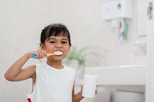 pequeña y linda niña limpiándose los dientes con un cepillo de dientes en el baño foto