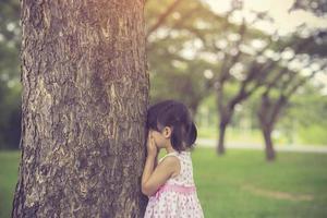 little girl is playing hide-and-seek hiding face in the park.Vintage color photo