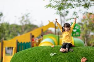 Cute Asian girl having fun trying to climb on artificial boulders at schoolyard playground, Little girl climbing up the rock wall, Hand Eye Coordination, Skills development photo