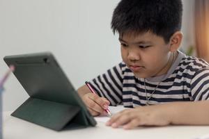Kid self isolation using tablet for his homework,Child doing using digital tablet searching information on internet during covid 19 lock down,Home schooling,Social Distance,E-learning online education photo