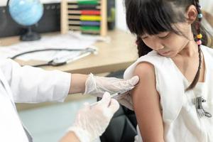 Vaccination concept. Female doctor vaccinating cute little girl in clinic photo