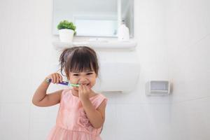 niñita linda limpiándose los dientes con cepillo de dientes en el baño foto