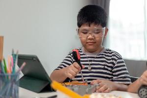 un joven estudiante de asia aprende de forma remota en línea en casa codificando un automóvil robot y un cable de placa electrónica en tallo, vapor, ingeniero matemático, ciencia, tecnología, código informático en robótica para niños. foto