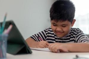 niño autoaislado usando tableta para su tarea, niño usando tableta digital buscando información en Internet durante el bloqueo de covid 19, educación en el hogar, distancia social, educación en línea de aprendizaje electrónico foto