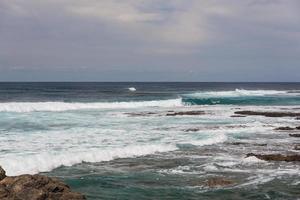 Turbulent ocean waves with white foam beat coastal stones photo