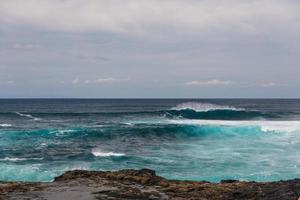 Turbulent ocean waves with white foam beat coastal stones photo