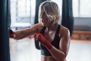 Right hand kick. Female boxer is punching the bag. Blonde have exercise in the gym photo