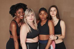 directamente a la cámara. grupo de mujeres multiétnicas de pie en el estudio con fondo marrón foto