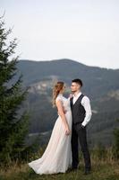 happy stylish bride and groom running and having fun in mountains on summer sunny day photo