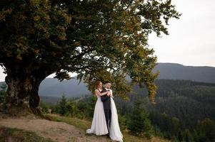 happy stylish bride and groom running and having fun in mountains on summer sunny day photo