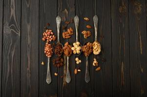 Hazelnut, cashews, raisins, almonds, peanuts, walnuts in silver spoons on a rustic background photo