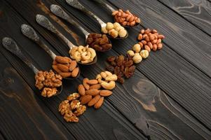 Hazelnut, cashews, raisins, almonds, peanuts, walnuts in silver spoons on a rustic background photo