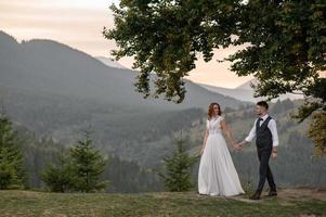 happy stylish bride and groom running and having fun in mountains on summer sunny day photo