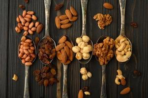 Hazelnut, cashews, raisins, almonds, peanuts, walnuts in silver spoons on a rustic background photo