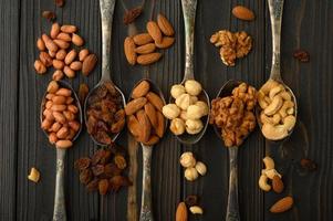 avellanas, anacardos, pasas, almendras, cacahuetes, nueces en cucharas de plata sobre un fondo rústico foto