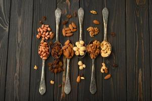Hazelnut, cashews, raisins, almonds, peanuts, walnuts in silver spoons on a rustic background photo